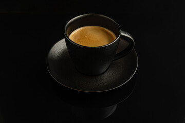 aromatic freshly brewed coffee in a black ceramic cup on a black mirroring surface