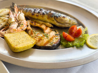 Grilled seafood platter with fish, shrimp, polenta, and vegetables on plate