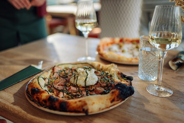 Gourmet pizza with burrata, pistachios and cooked ham served on restaurant table