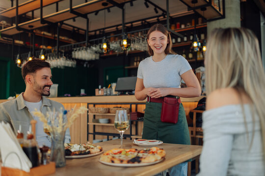 Smiling waitress taking order from customers in pizzeria restaurant