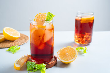 Fototapeta premium Iced tea with lemon and ice in a tall glass on a white background. The concept of a refreshing drink or lemonade on a hot summer day. Front view and copy space.