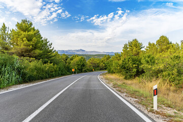 A winding asphalt road curves gently through a green countryside landscape under a vibrant blue sky...