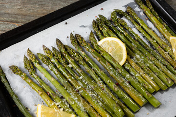 Baked green asparagus with lemon on baking tray and hard cheese