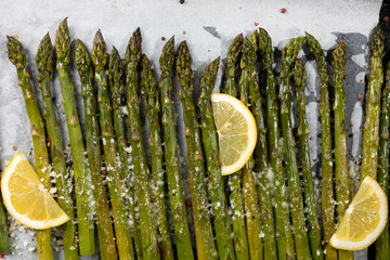 Baked green asparagus with lemon on baking tray and hard cheese top view