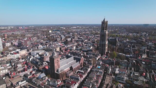 Approach aerial city center Utrecht, The Netherlands, on a bright sunny day with church and cathedral rising above the low build picturesque canal homes. Urban development and holland flat landscape