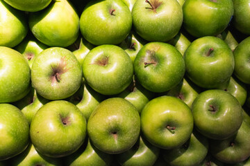 A vibrant display of fresh green apples stacked closely together in supermarket, showcasing their crisp texture, glossy skin, and tart, juicy appeal under bright lighting.
