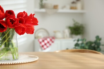 Beautiful red tulips in vase on wooden table indoors, closeup. Space for text