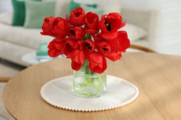 Beautiful red tulips in vase on wooden table indoors