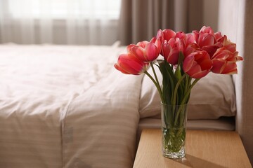 Bouquet of beautiful tulips on side table in bedroom. Space for text