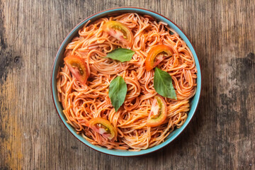 spaghetti bolognese in a plate with sliced ​​tomatoes and basil leaves on wooden table