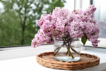 Beautiful lilac flowers in glass vase on window sill indoors, closeup. Space for text