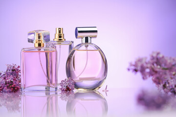 Bottles of perfume and lilac flowers on mirror surface against violet gradient background,...