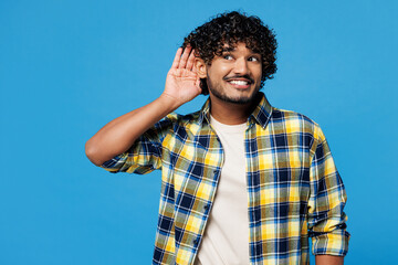 Young happy curious nosy Indian man he wear yellow checkered shirt casual clothes try to hear you...