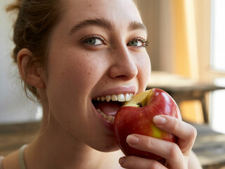A close-up photograph of a young woman biting into a crisp, red apple