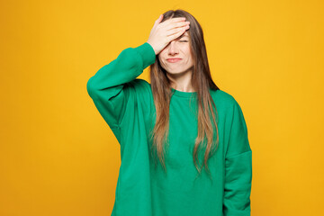 Young sad shocked woman she wear green sweatshirt casual clothes put hand on face facepalm epic fail mistaken omg gesture isolated on plain yellow orange background studio portrait. Lifestyle concept.