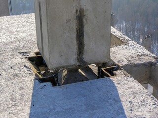 Detailed view showing the concrete pillar and its metal base at the construction site on a sunny day.