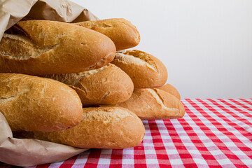 Fresh baguettes in brown paper bag on red checkered tablecloth
