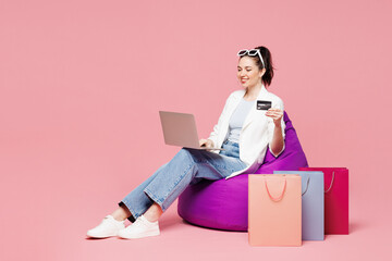 Full body young woman wear white clothes sit in bag chair near shopping paper package bags use...