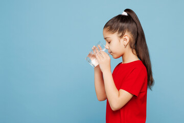 Side view little kid girl 8-9 years old wearing red t-shirt have fun drink water hold glass...