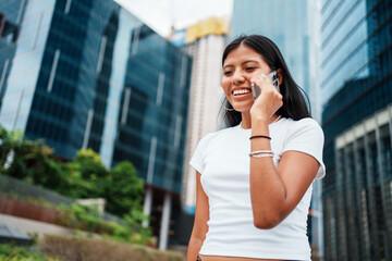 A Smiling Young Woman Engaged in a Lively Phone Conversation in a Bustling Urban Setting