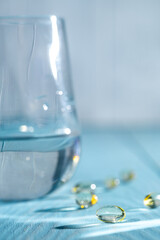 Soft Gyls and fish oil, vitamin D capsules are located near a glass of water, against a blue background, emphasizing the importance of health and well -being in daily nutrition