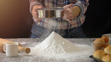 Artisan bread dough preparation. Use sieve or colander to sift flour into pile of flour for handmade bread with bakery equipment tool, black background. professional baker process at work.
