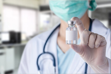 close up of glass bottle with blank white label for vaccine in doctor's gloved hand, blurry laboratory at background. concept of vaccine and medicine research for disease prevention at lab