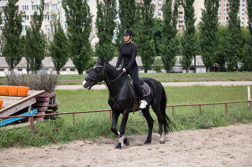 A girl learns to ride a black horse. Sunny summer day.