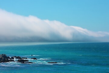 Misty white fog rolling on teal ocean skyline  
