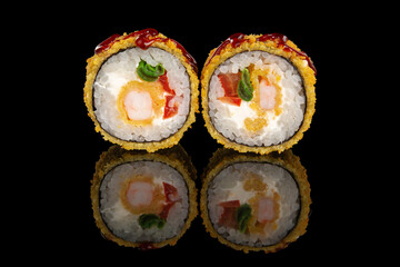 Deep fried sushi roll filled with shrimp, cream cheese, red bell pepper and greens. Served on a black reflective surface for a vibrant and modern food presentation