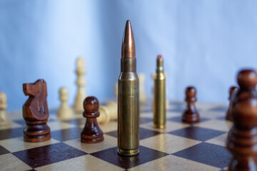 Rifle bullet placed vertically on a chessboard among chess pieces, illustrating the abstract...