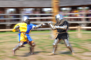 Two knights in shining armor clash swords during a historical reenactment event. motion blurred