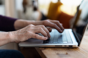 Senior woman typing on laptop keyboard at home office: working remotely