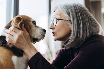 Senior woman gently talking to her beagle dog at home