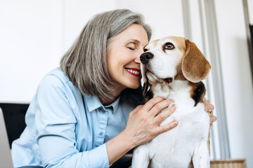Happy senior woman expressing love and affection to beagle dog at home