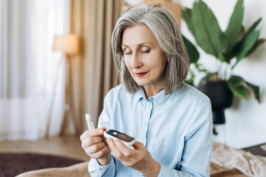 Senior woman checking blood sugar level with glucometer at home