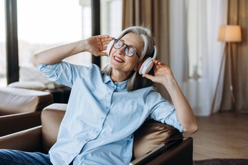 Happy senior woman listening music with wireless headphones at home