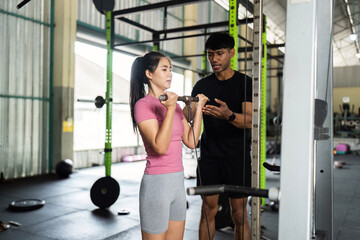 Fitness Training. A coach assists a woman with her weightlifting technique at the gym.
