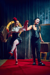 Fototapeta premium Joyful cabaret couple walks forward holding hands smiling in red gloves and hat with suitcases. Concept of cabaret, retro, lifestyle, performance, humor, show, celebration, theater, circus.