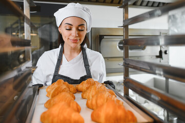 Baker woman holding tray of freshly baked croissants in bakery