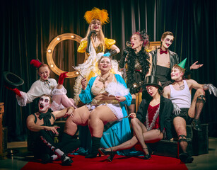 Group of artistic people, cabaret performers in eccentric outfits and makeup, pose on red carpet...