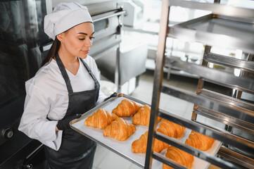 Baker woman holding tray of freshly baked croissants in bakery