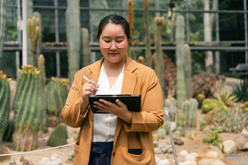 Woman plant scientist with stylus and tablet analyzing cactus varieties in botanical greenhouse....