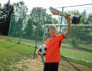 Happy Boy Celebrating Victory with Soccer Ball and Trophy at the Stadium. Winning and the spirit of competition. Childhood, sports, success, an active lifestyle. 