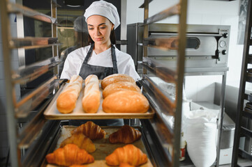 Baker placing tray of freshly baked bread and croissants in bakery oven