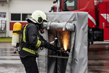 Fototapeta premium Firefighter in full gear creates sparks while cutting metal inside a protected booth during a rainy outdoor training exercise