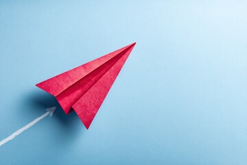 Red paper airplane, symbolic of ambition and progress, directed by a chalk arrow on a light blue background