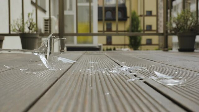 Shattering wine glass hitting wooden floor in slow motion, A wine glass breaks on impact with a wooden deck surface, captured at the moment of shattering
