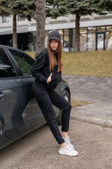 Fototapeta premium Cute girl model in a sporty comfortable casual black outfit with a hoodie and sweatpants posing shows a quality ot clothing