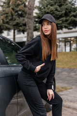Cute girl model in a sporty comfortable casual black outfit with a hoodie and sweatpants posing shows a quality ot clothing